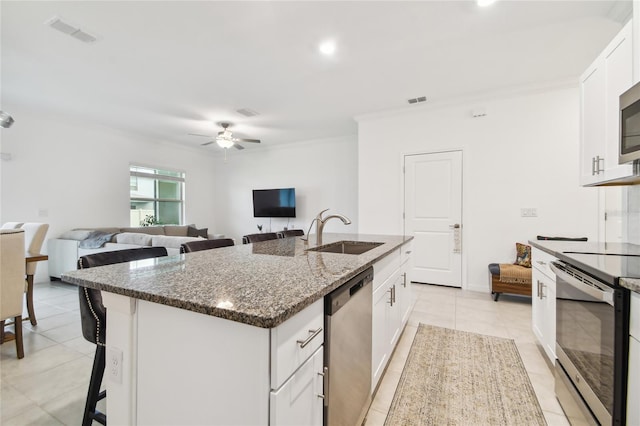 kitchen with sink, appliances with stainless steel finishes, dark stone counters, a kitchen island with sink, and white cabinets