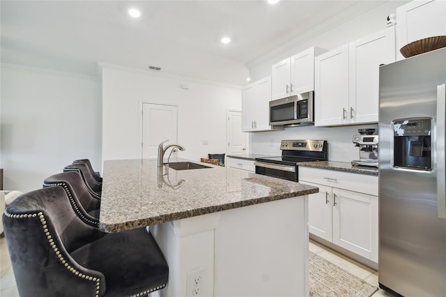 kitchen featuring white cabinetry, appliances with stainless steel finishes, a kitchen breakfast bar, an island with sink, and dark stone counters