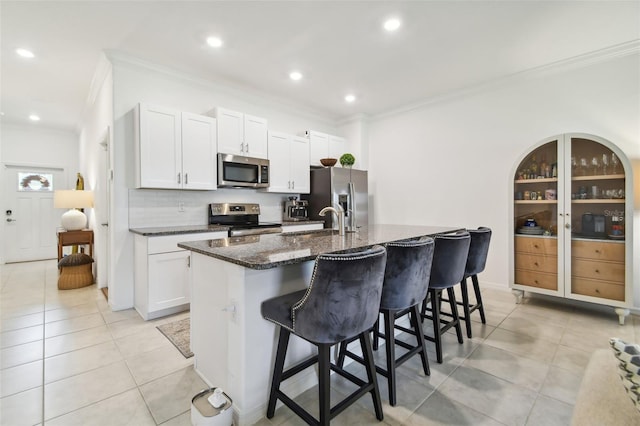 kitchen with a breakfast bar, white cabinetry, dark stone counters, stainless steel appliances, and a center island with sink