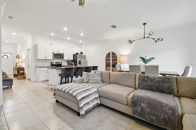 tiled living room featuring ornamental molding and a chandelier