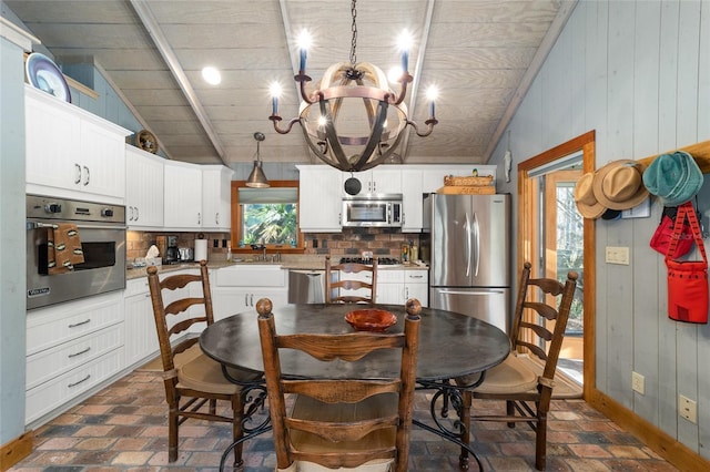 dining room featuring lofted ceiling, sink, wooden walls, and an inviting chandelier