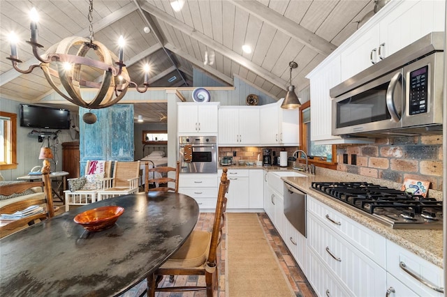 kitchen with sink, appliances with stainless steel finishes, white cabinetry, light stone counters, and decorative light fixtures