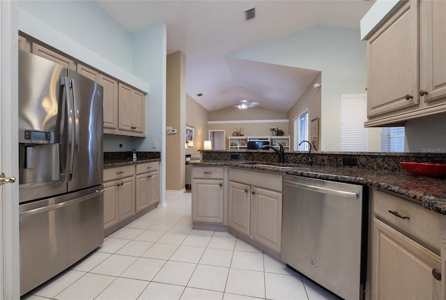 kitchen with dark stone countertops, vaulted ceiling, stainless steel appliances, and light tile patterned flooring