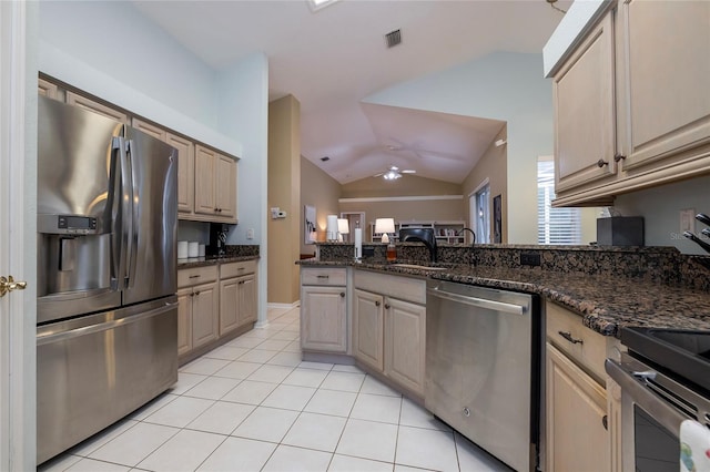 kitchen featuring lofted ceiling, light tile patterned floors, appliances with stainless steel finishes, ceiling fan, and dark stone counters