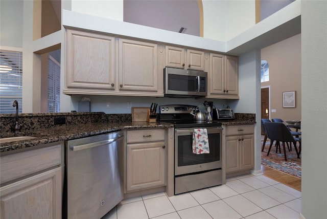 kitchen featuring sink, light tile patterned floors, dark stone countertops, a towering ceiling, and stainless steel appliances