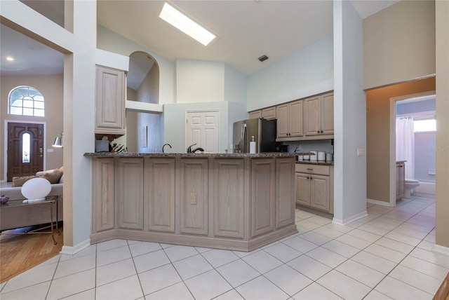 kitchen featuring stainless steel fridge, a high ceiling, kitchen peninsula, light tile patterned flooring, and dark stone counters