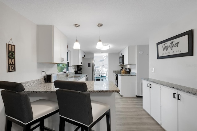 kitchen featuring white cabinets, appliances with stainless steel finishes, light hardwood / wood-style flooring, and pendant lighting