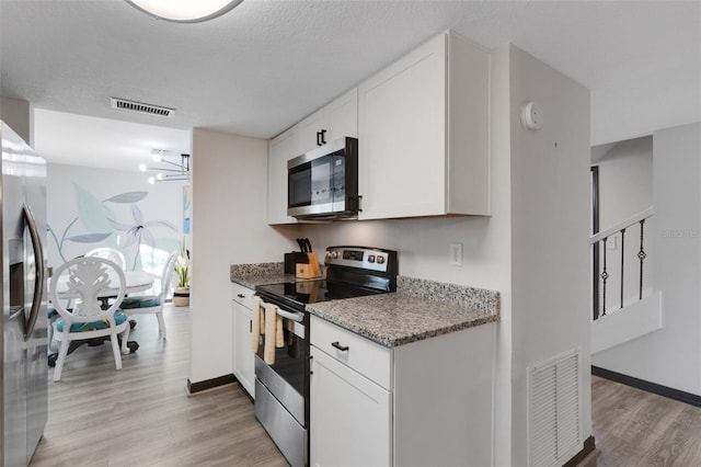 kitchen with light stone countertops, appliances with stainless steel finishes, light hardwood / wood-style flooring, a notable chandelier, and white cabinets