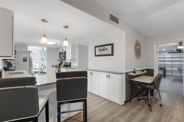 kitchen with appliances with stainless steel finishes, sink, light hardwood / wood-style flooring, white cabinetry, and hanging light fixtures