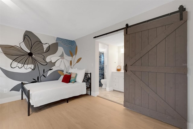 bedroom featuring wood-type flooring, a barn door, and ensuite bath