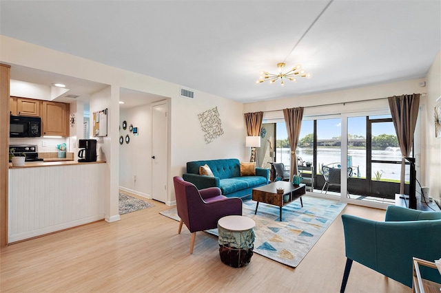 living room featuring light wood-type flooring, a chandelier, and a water view