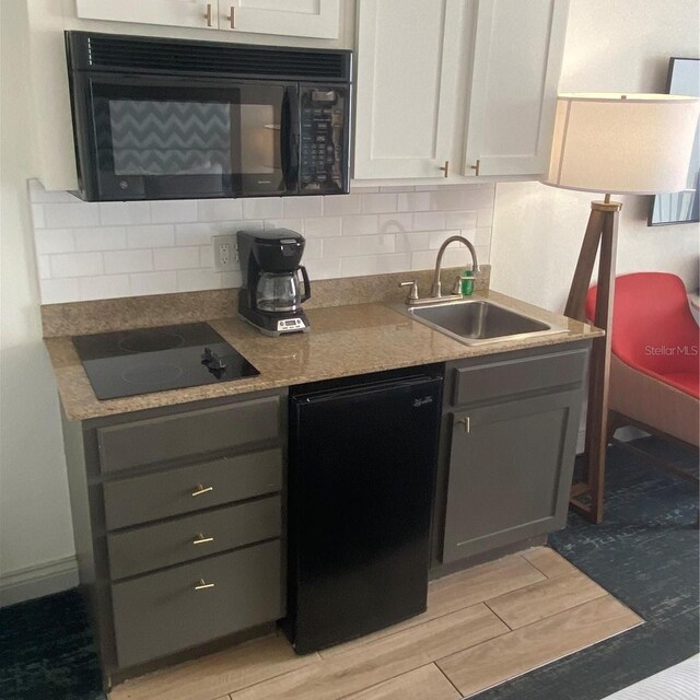 kitchen with black appliances, light hardwood / wood-style flooring, tasteful backsplash, sink, and white cabinets