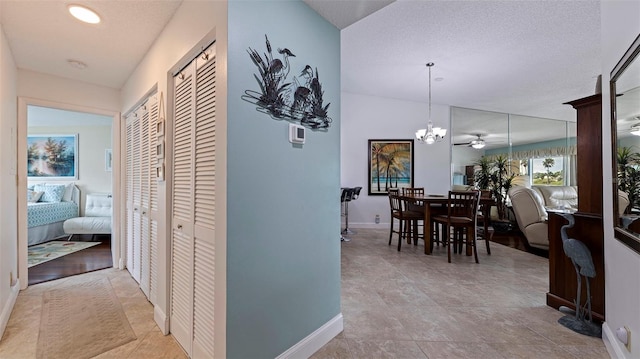 corridor featuring a textured ceiling, light tile patterned floors, lofted ceiling, and a chandelier