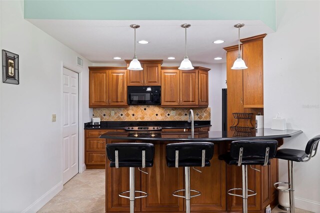 kitchen featuring dark countertops, black microwave, hanging light fixtures, and a kitchen bar