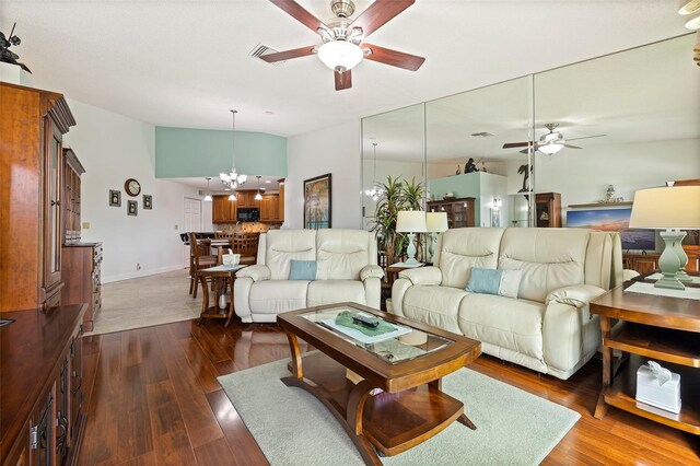 living room featuring baseboards, visible vents, dark wood-type flooring, vaulted ceiling, and ceiling fan with notable chandelier