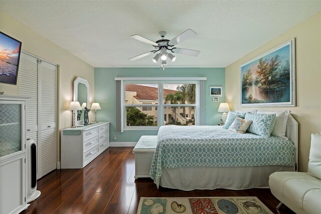 bedroom with a ceiling fan, a textured ceiling, baseboards, and dark wood-style flooring