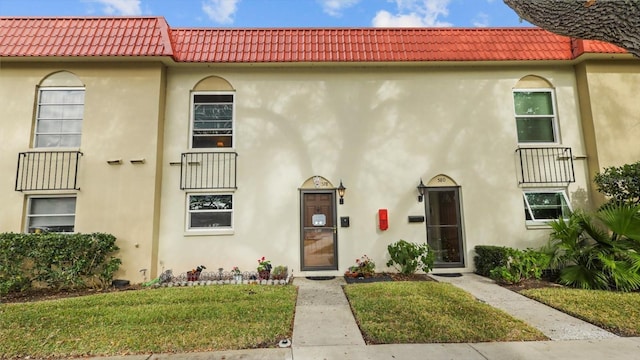 view of front of house featuring a tile roof, a front yard, and stucco siding