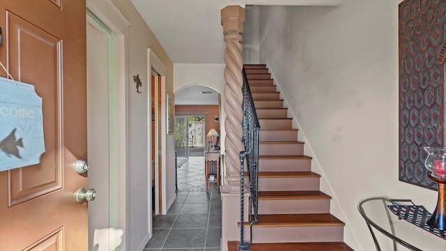 foyer entrance with arched walkways, stairway, baseboards, and dark tile patterned floors