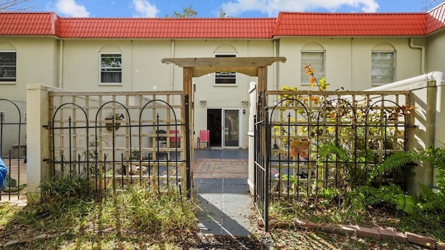 doorway to property featuring a tile roof, a gate, fence, and stucco siding