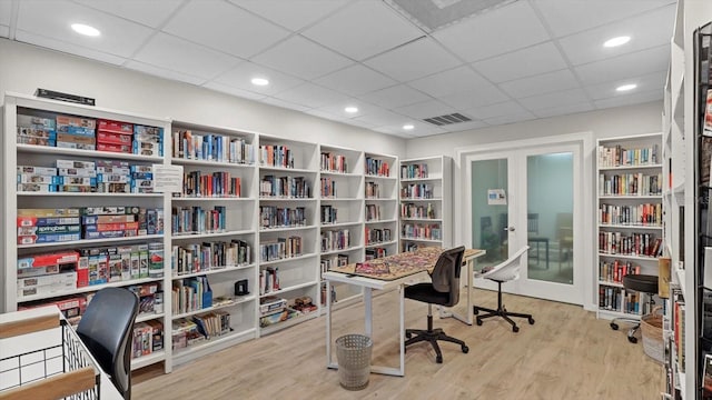 office with french doors, visible vents, wall of books, and wood finished floors