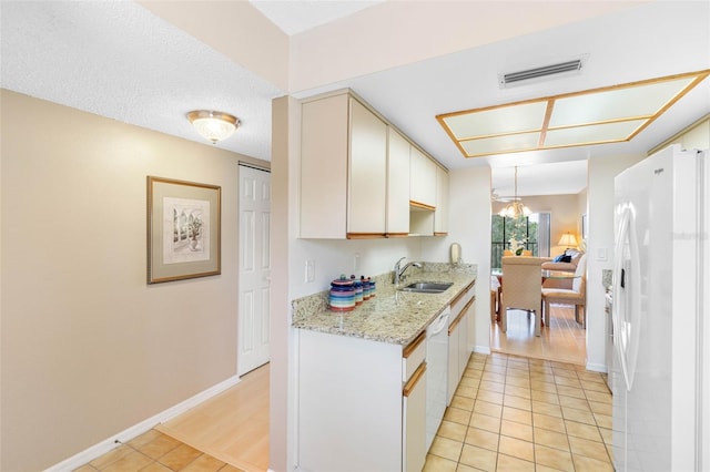 kitchen featuring light tile patterned floors, light stone counters, white appliances, a sink, and visible vents