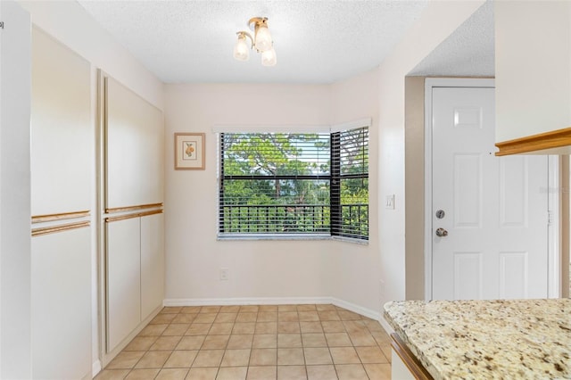 interior space featuring light tile patterned floors, baseboards, and a textured ceiling