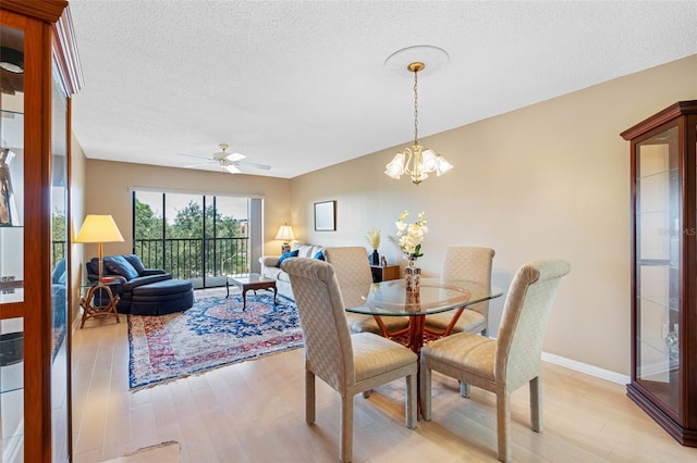 dining space with baseboards, light wood-style flooring, a textured ceiling, and ceiling fan with notable chandelier