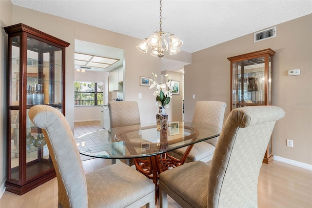 dining area with a textured ceiling, light wood-style flooring, visible vents, baseboards, and an inviting chandelier