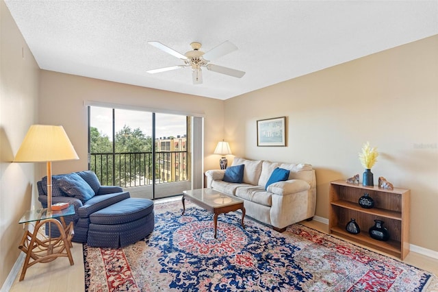 living area with light wood-type flooring, ceiling fan, a textured ceiling, and baseboards