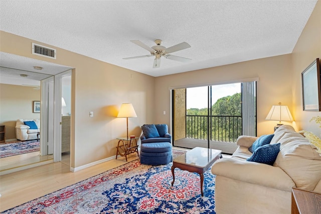 living area with visible vents, ceiling fan, a textured ceiling, light wood-type flooring, and baseboards