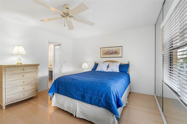 bedroom featuring baseboards, ensuite bath, a ceiling fan, and wood finished floors