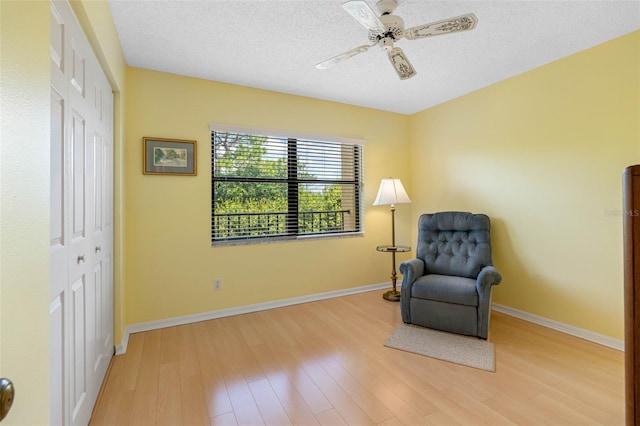 sitting room featuring a textured ceiling, baseboards, and light wood-style floors