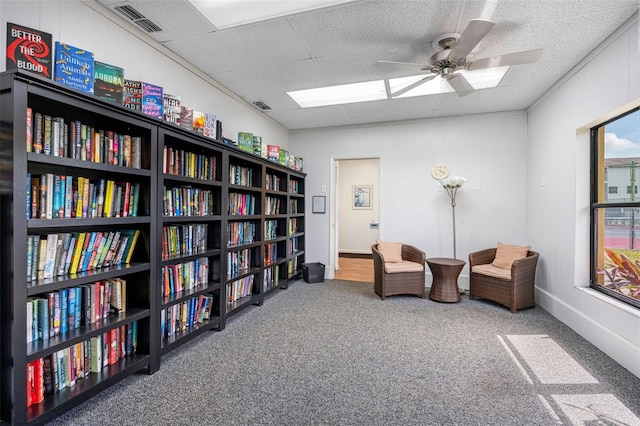 sitting room featuring carpet floors, visible vents, bookshelves, and a ceiling fan