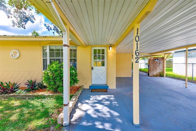 property entrance with an attached carport, fence, and stucco siding