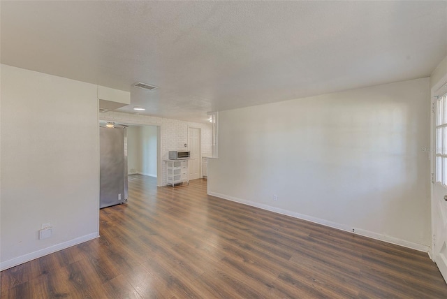 empty room featuring a textured ceiling, dark wood-style flooring, visible vents, and baseboards