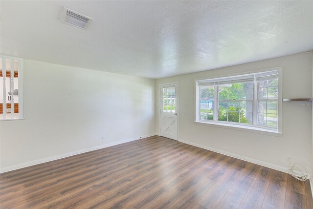 spare room with baseboards, a textured ceiling, visible vents, and dark wood-style flooring