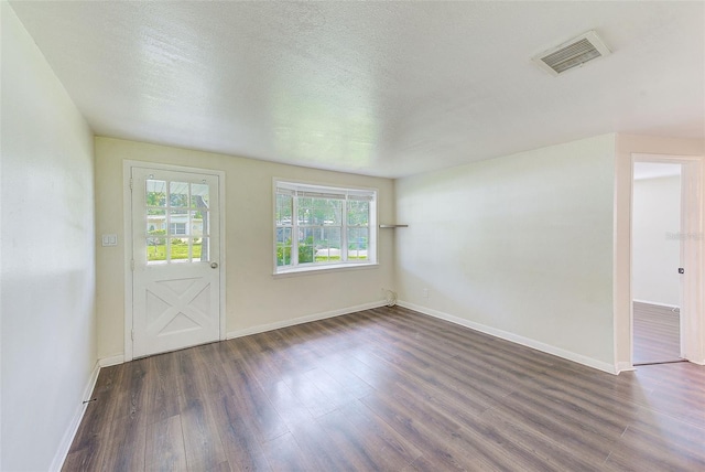 empty room featuring a textured ceiling, dark wood-style flooring, visible vents, and baseboards