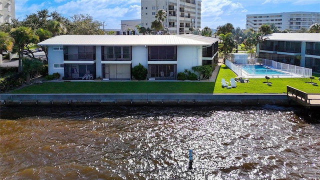 rear view of house featuring a water view, a fenced in pool, and a lawn