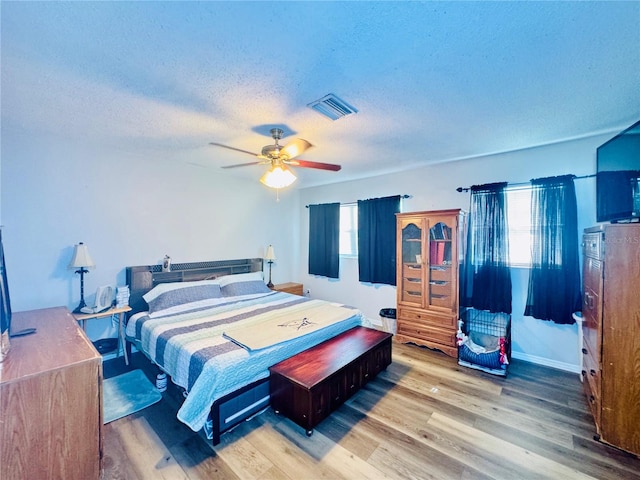 bedroom featuring multiple windows, a textured ceiling, light hardwood / wood-style floors, and ceiling fan