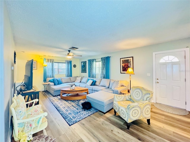 living room with ceiling fan, light wood-type flooring, and a textured ceiling