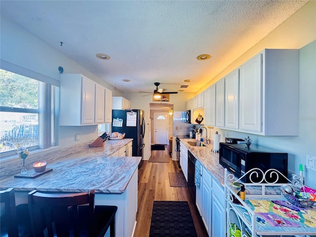 kitchen featuring light wood-type flooring, a sink, a textured ceiling, freestanding refrigerator, and white cabinets