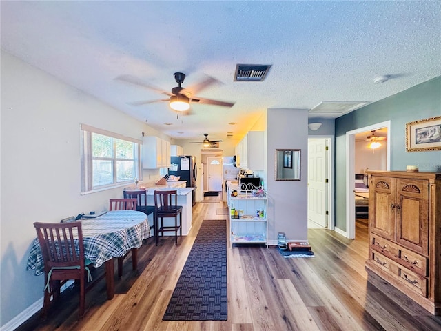 bedroom with a textured ceiling, stainless steel fridge, ceiling fan, and light wood-type flooring