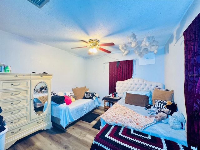 bedroom with ceiling fan, wood-type flooring, and a textured ceiling