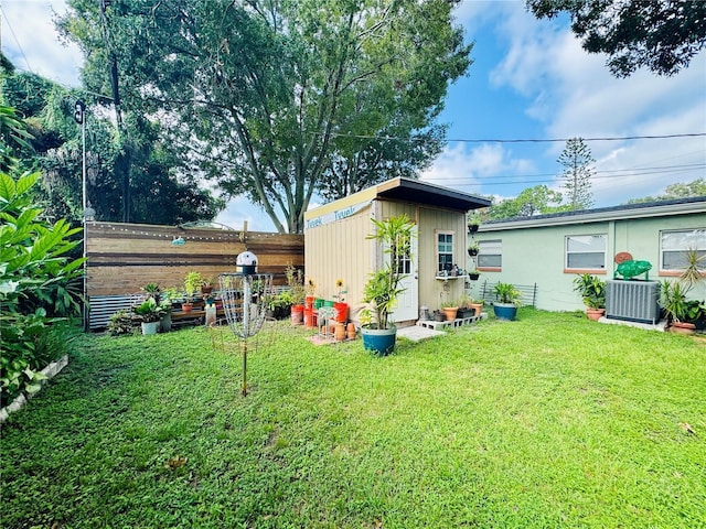 rear view of house with central AC, fence, a yard, a storage shed, and an outdoor structure