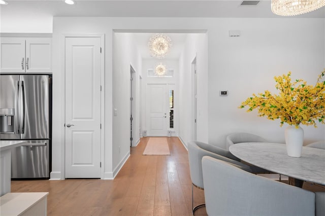 kitchen with light wood-type flooring, an inviting chandelier, white cabinetry, and stainless steel refrigerator with ice dispenser