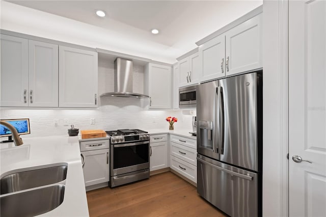 kitchen with appliances with stainless steel finishes, light hardwood / wood-style flooring, wall chimney exhaust hood, white cabinets, and sink