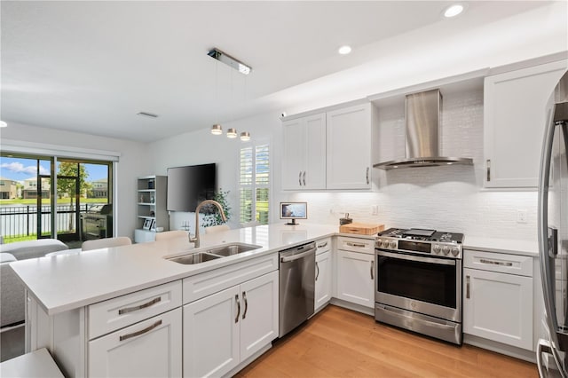 kitchen featuring kitchen peninsula, wall chimney range hood, light wood-type flooring, stainless steel appliances, and sink