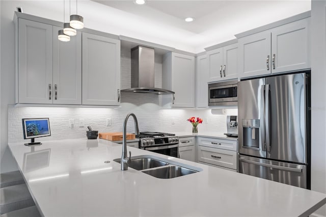 kitchen featuring pendant lighting, appliances with stainless steel finishes, sink, decorative backsplash, and wall chimney range hood