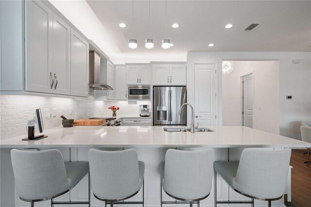 kitchen with appliances with stainless steel finishes, hardwood / wood-style flooring, wall chimney exhaust hood, backsplash, and sink