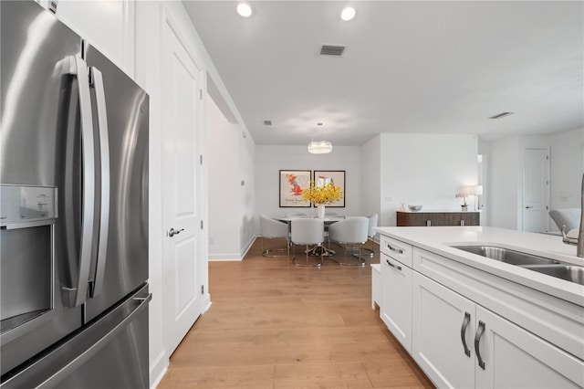 kitchen with white cabinetry, light hardwood / wood-style flooring, decorative light fixtures, stainless steel refrigerator with ice dispenser, and sink